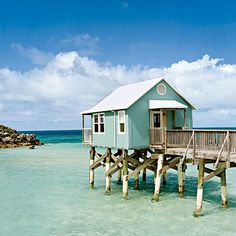 a small blue house sitting on top of a wooden pier next to the ocean with clear water