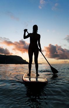 a woman standing on top of a surfboard in the ocean with a oar