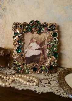 an old fashion picture frame with pearls and other accessories on a lace doily next to a mirror