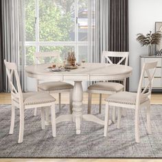 a white table and chairs in front of a window with curtains on the windowsill