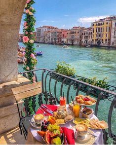 an outdoor table with food and drinks on it next to the water in venice, italy