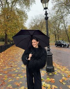 a woman standing under an umbrella in the rain with leaves on the ground around her