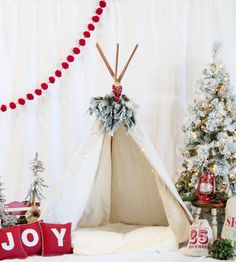 a teepee surrounded by christmas trees and other holiday decorations, with the word joy written on it