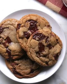 three chocolate chip cookies on a white plate with a red and white checkered tablecloth