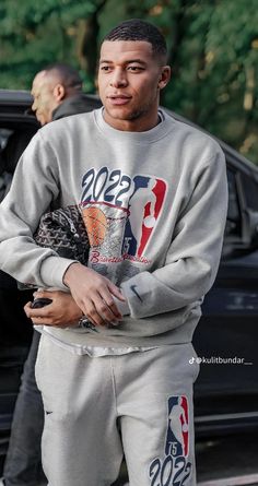 a man in grey sweatshirt and pants standing next to a car