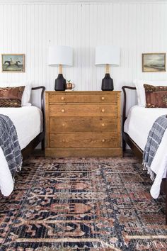 two twin beds in a bedroom next to a dresser with lamps on top of it