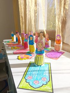 paper dolls are sitting on top of a table in front of a window with curtains