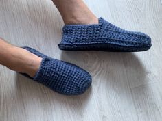 a person's feet wearing slippers on top of a white wooden floor next to a pair of blue crocheted shoes