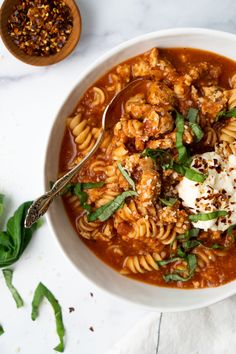 a white bowl filled with pasta and meat covered in sauce, garnished with parmesan cheese