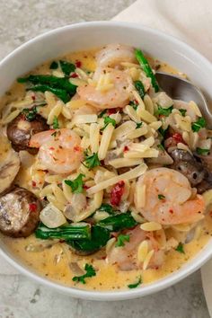 a white bowl filled with pasta and shrimp on top of a marble counter next to a napkin