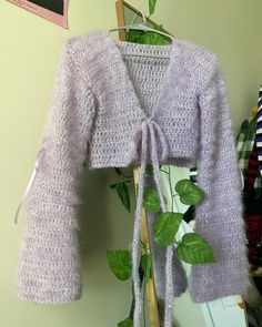 a purple knitted sweater hanging up on a clothes rack next to a green plant