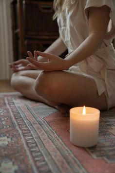 a woman sitting on the floor in front of a candle