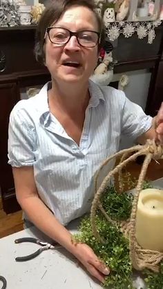 a woman is holding a candle in front of some moss and scissors on a table