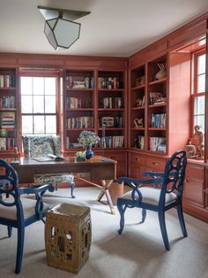 an office with red bookcases and blue chairs in front of a large window