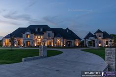 a large house with lots of windows and lights on it's front entrance at dusk