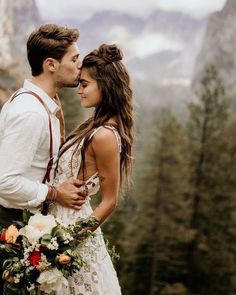 a man and woman standing next to each other in front of mountains with flowers on them