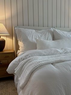 a bed with white comforter and pillows in a bedroom next to a night stand