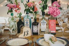 the table is set with wine bottles and flowers in vases, plates and silverware