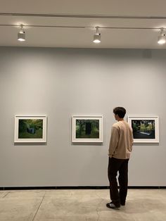 a man standing in front of three pictures on a wall with lights above him and looking at them