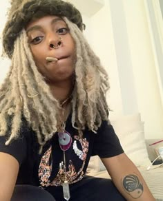 a woman with dreadlocks sitting on a couch wearing a black shirt and hat