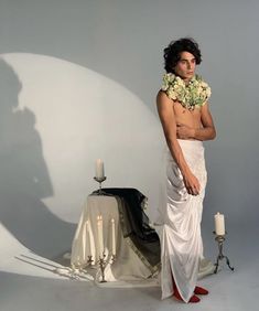 a man standing in front of a table with candles and flowers on his head, wearing a white sarong