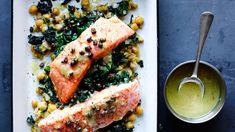 two salmons on a platter with vegetables and sauce next to a bowl of dressing