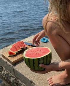 a woman cutting up a watermelon on the edge of a pier