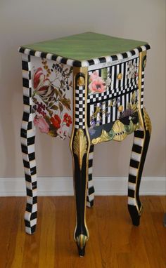 an ornately painted table with flowers and stripes on the top, against a white wall