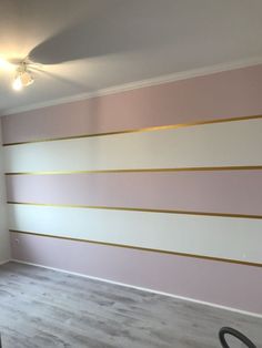 an empty room with pink and gold stripes painted on the wall behind a black vacuum