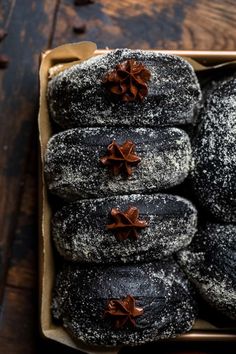 a box filled with black and white donuts covered in powdered sugar on top of a wooden table