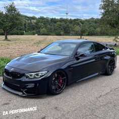 a black car parked on the side of a road next to some grass and trees