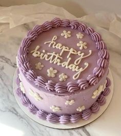 a birthday cake with purple frosting and white flowers on the top that says happy birthday