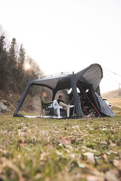 two people sitting in a tent on the grass