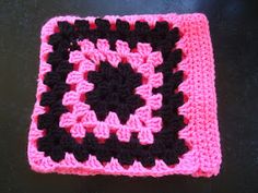 a crocheted square with black and pink squares on the center, sitting on a table