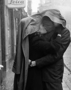 an old man and woman kissing in the rain on a city street with a train passing by