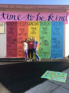 three girls standing in front of a rainbow colored sign that says time to be kinder