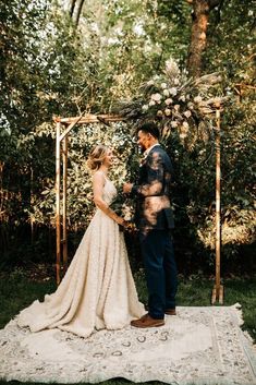 a bride and groom standing in front of an outdoor ceremony arch with flowers on it