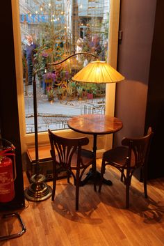 a table and two chairs in front of a window with a lamp on top of it