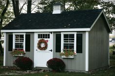 a small shed with two wreaths on the door and flowers in the window boxes