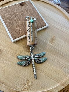 a dragonfly charm sitting on top of a wooden table next to a bottle opener