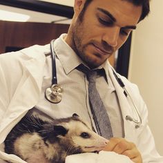 a man in a white shirt and tie holding a ferret while wearing a stethoscope