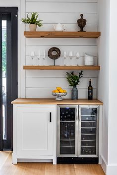 a white kitchen with open shelving and wine glasses on the counter top, next to a black door