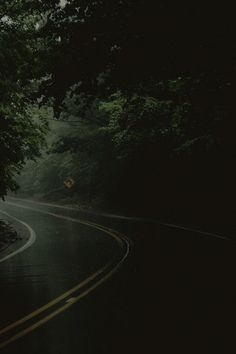 an empty road in the dark with trees on both sides and a yellow street sign