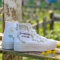 a pair of white sneakers with embroidered flowers on them sitting on a bench in front of yellow flowers