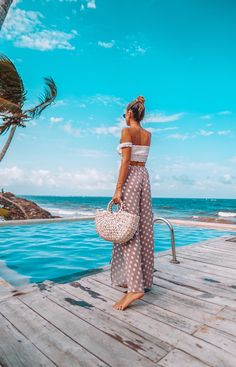 a woman standing on a dock looking out at the ocean with palm trees in the background