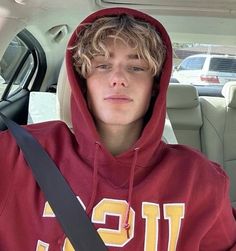 a young man sitting in the back seat of a car wearing a red hoodie