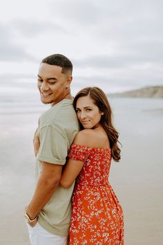 a man and woman standing next to each other on the beach with water in the background