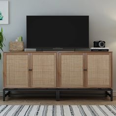 a flat screen tv sitting on top of a wooden cabinet next to a rug and potted plant