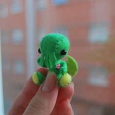 a small green stuffed animal sitting on top of a persons finger