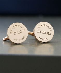 two personalized cufflinks with names and date engraved on the backs, sitting on a table